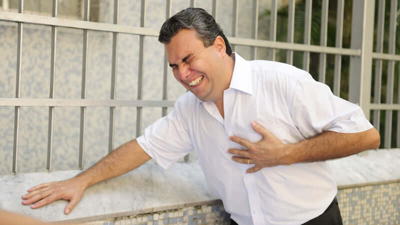 Magnesium Most Not Getting Enough, Man in white shirt grabbing his chest, expressing discomfort and pain while standing outside.