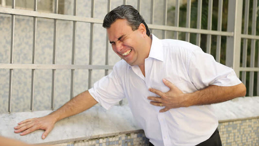 Magnesium Most Not Getting Enough, Man in white shirt grabbing his chest, expressing discomfort and pain while standing outside.
