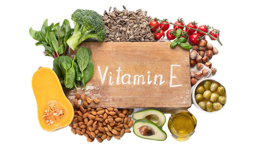 An assortment of foods rich in Vitamin E, including nuts, greens, and seeds, with a wooden sign displaying 'Vitamin E'.
