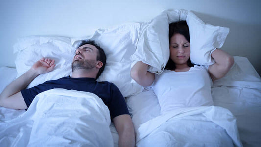 couple in bed with man sleeping peacefully and woman covering ears, related to How Tryptophan Was Banned