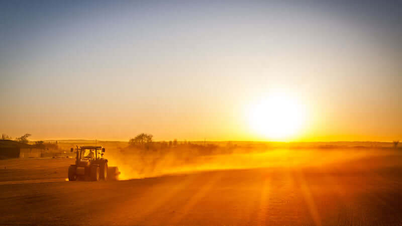 Movie A Thousand Suns: A tractor working in a sunlit field at sunset, creating a dusty atmosphere.