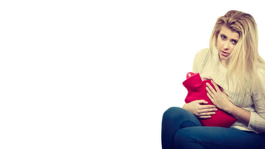 Woman holding a hot water bottle experiencing discomfort from Pre Menstrual Syndrome.