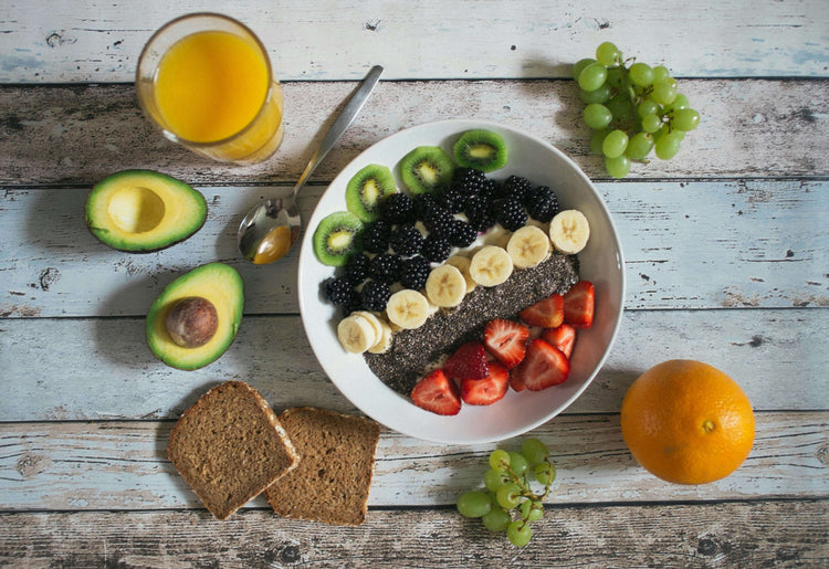 Bowl of chia seeds topped with bananas, strawberries, blackberries, kiwi, orange juice, and avocado on a rustic table.