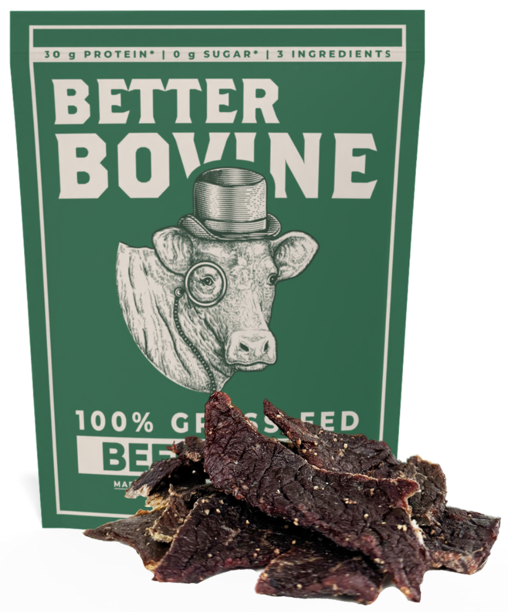 A package of Better Bovine beef jerky stands upright against a plain white background, with several dark brown jerky slices piled in front of the box. The package is dark green with white text and an illustration of a cow wearing a top hat and monocle.