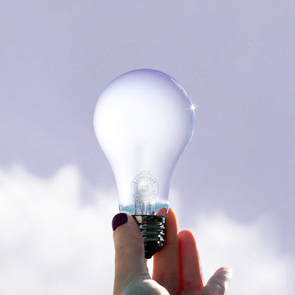Hand holding a light bulb against a clear sky