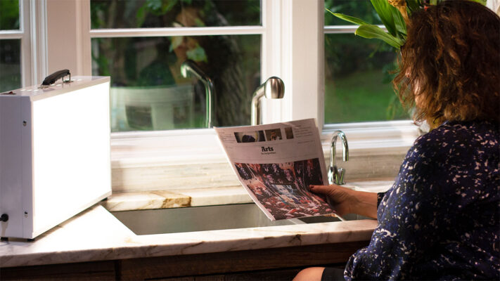 Person reading a magazine by a window with a sink and faucet in the foreground