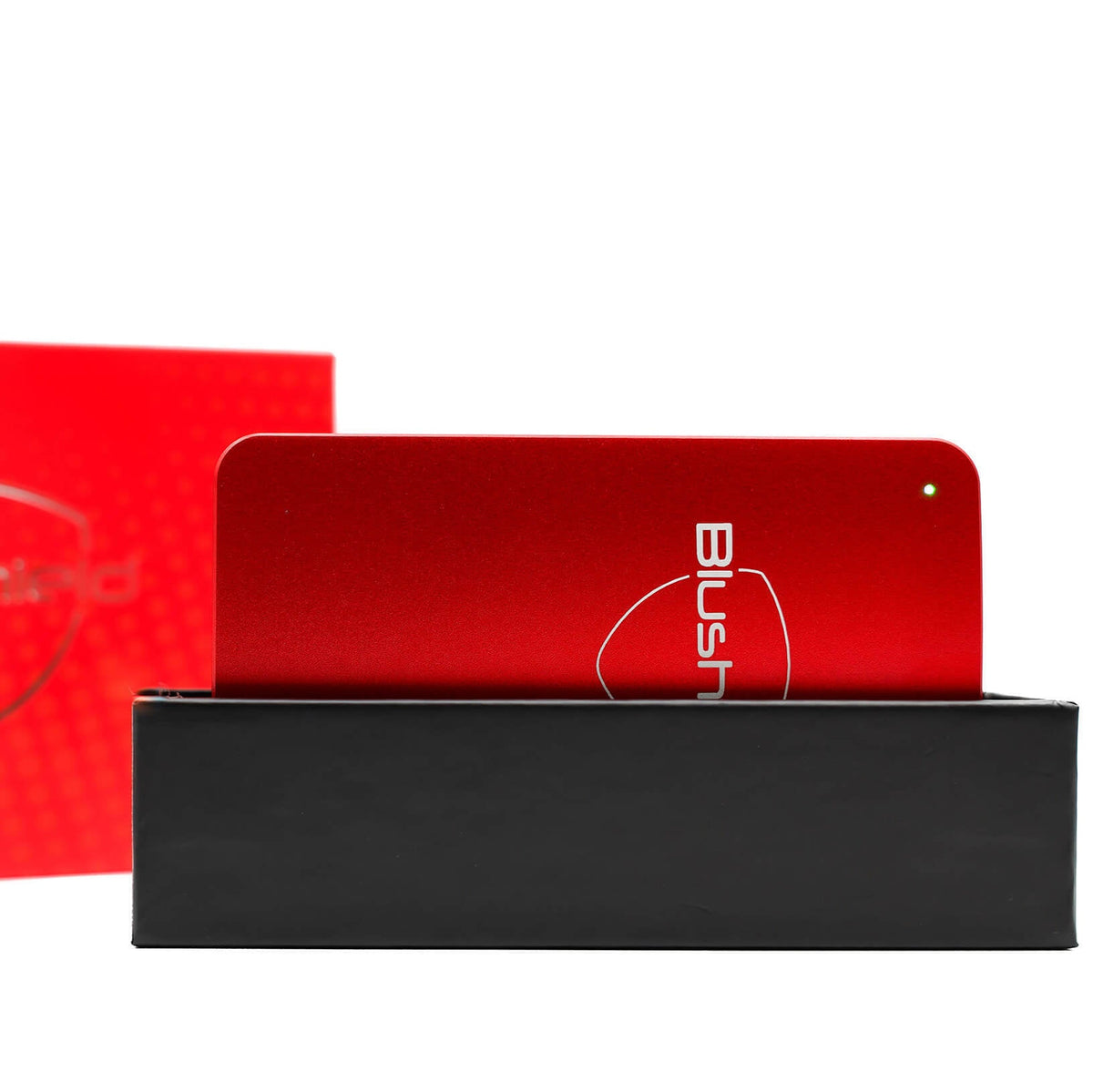 A red metal eyeglasses case or accessory with a white outlined logo reading BUSH, displayed above a black rectangular box on a white background. A red patterned box is partially visible on the left.