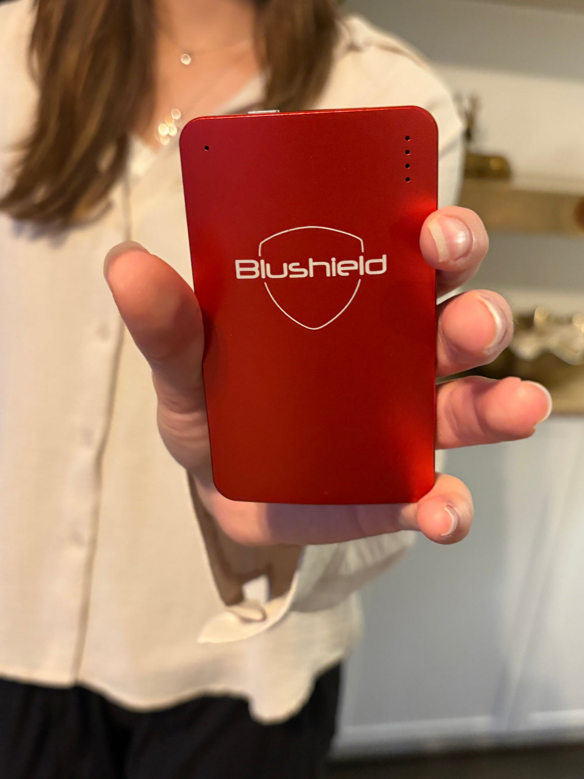 A person holding a red rectangular electronic device with the Blushield logo printed in white on the front.