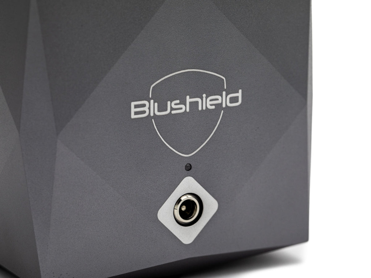 Close-up of a dark gray Blushield electronic device with a white shield logo and a circular port on a white background.