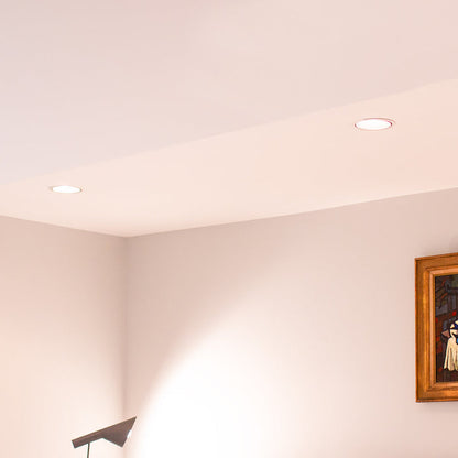 Two round recessed ceiling lights installed on a white ceiling in a minimalist room with light beige walls and a framed painting partially visible on the right.