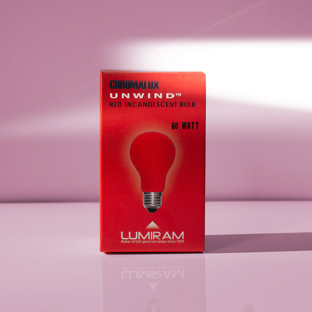 A red box of Lumiram Unwind 60 Watt Chromalux red incandescent light bulbs, standing on a reflective pink surface against a pink background.