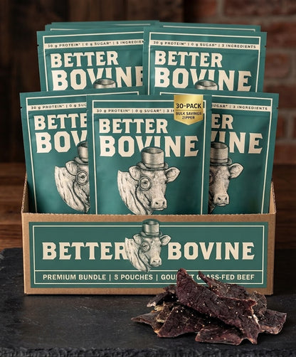 A display box filled with multiple Better Bovine beef tallow pouches, with a few dried beef jerky slices placed in front on a dark tabletop against a rustic brick background.