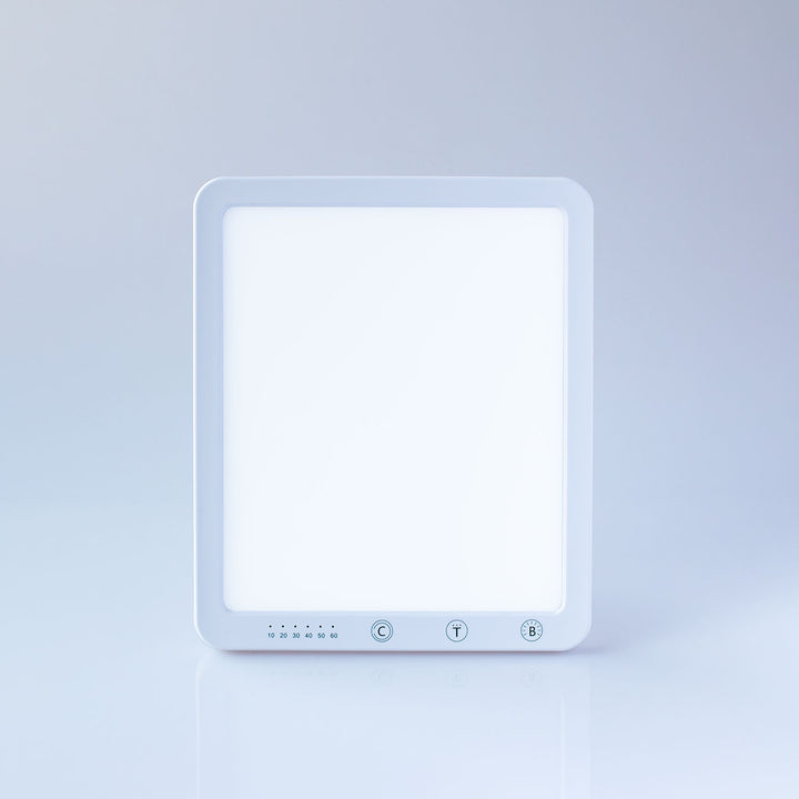A square white LED light panel with a glowing white face and three control buttons at the bottom, set against a clean light gray studio background.