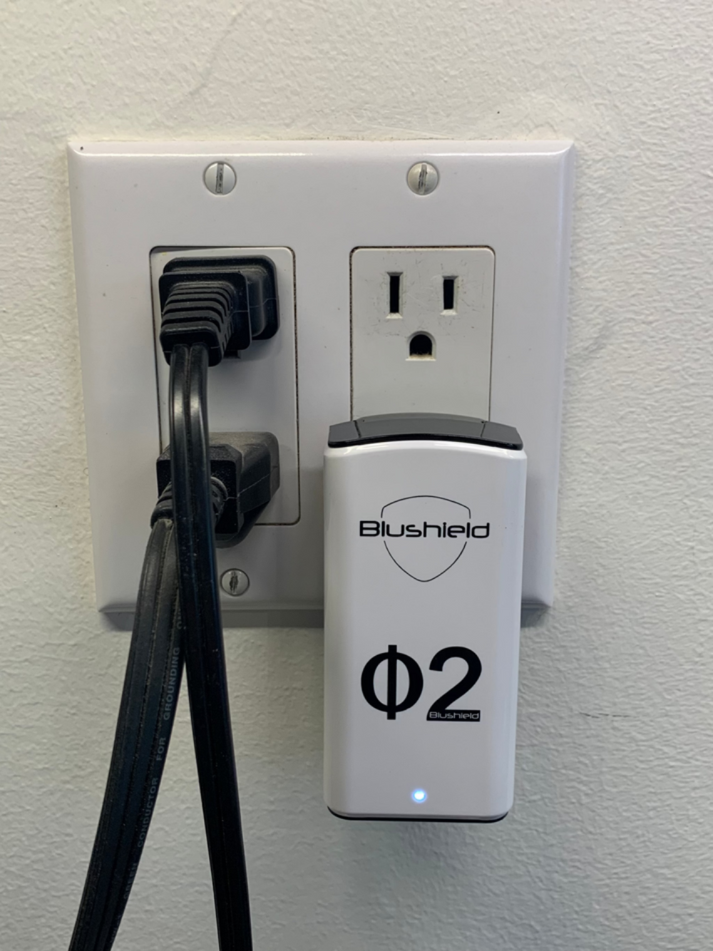 Blushield Φ2 device plugged into a wall outlet with a cable.