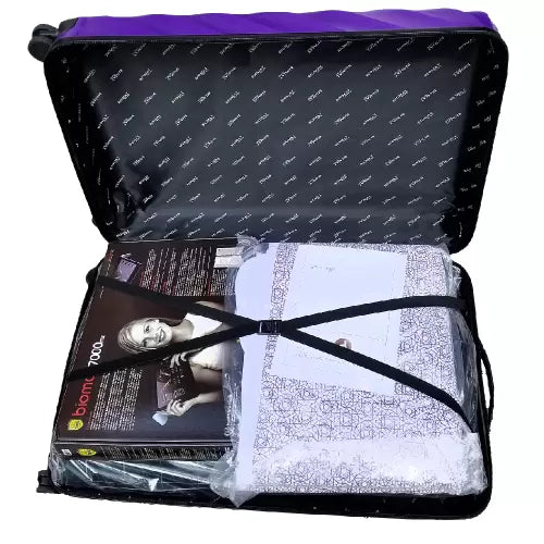 An open black zippered carrying case with a purple top lining, shown against a white background. Inside, a packaged product bundle is secured with a black elastic strap, including a printed insert card and a white patterned item wrapped in clear plastic.