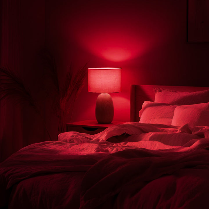 Bedroom with red lighting, featuring a lamp on a nightstand.