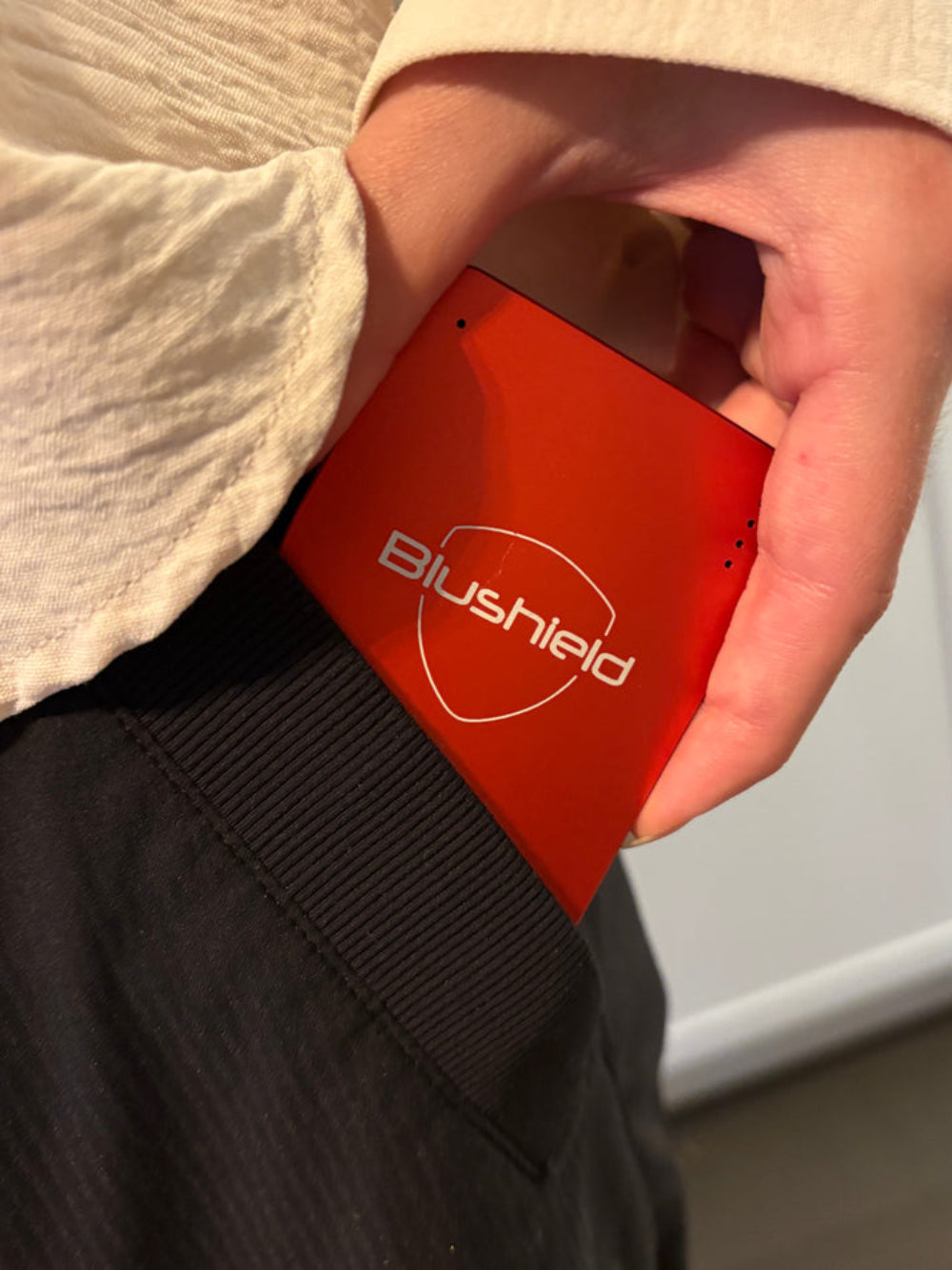Red Blushield product held in a hand with a blurred background