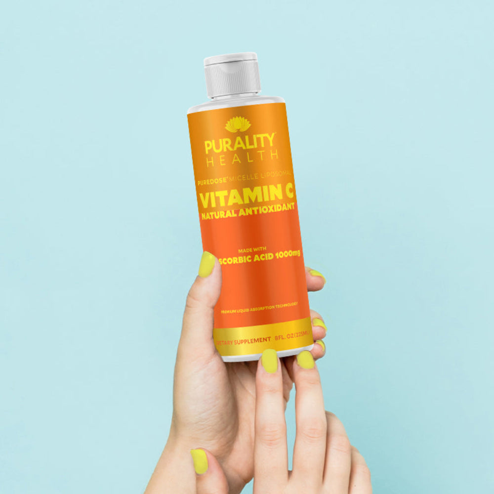 Hand holding a bottle of Purity Health Vitamin C supplement against a light blue background
