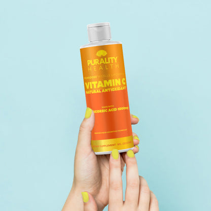 Hand holding a bottle of Purity Health Vitamin C supplement against a light blue background