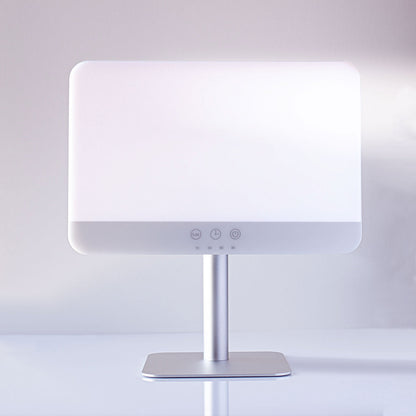 A modern LED vanity mirror with a glowing white illuminated faceplate, a slim silver metal stand, and a square base, shown on a clean white surface against a soft gray background.