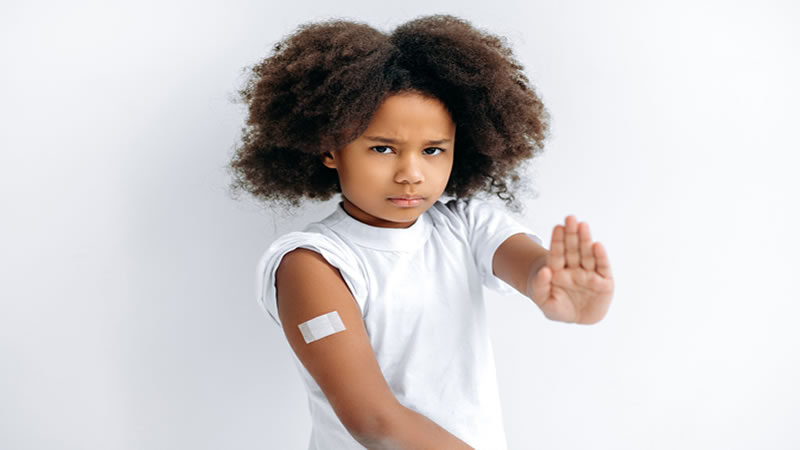 child with bandage on arm, holding hand up to stop more vaccines